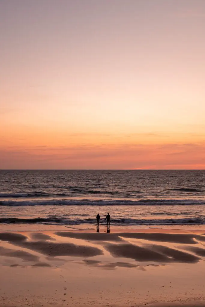 two people silhouetted on a beach at sunset
