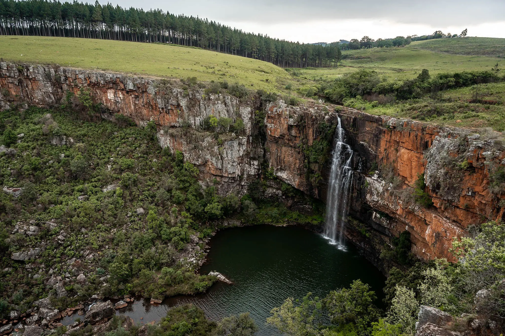 waterfall plunging into a dark pool surrounded by cliffs and forest