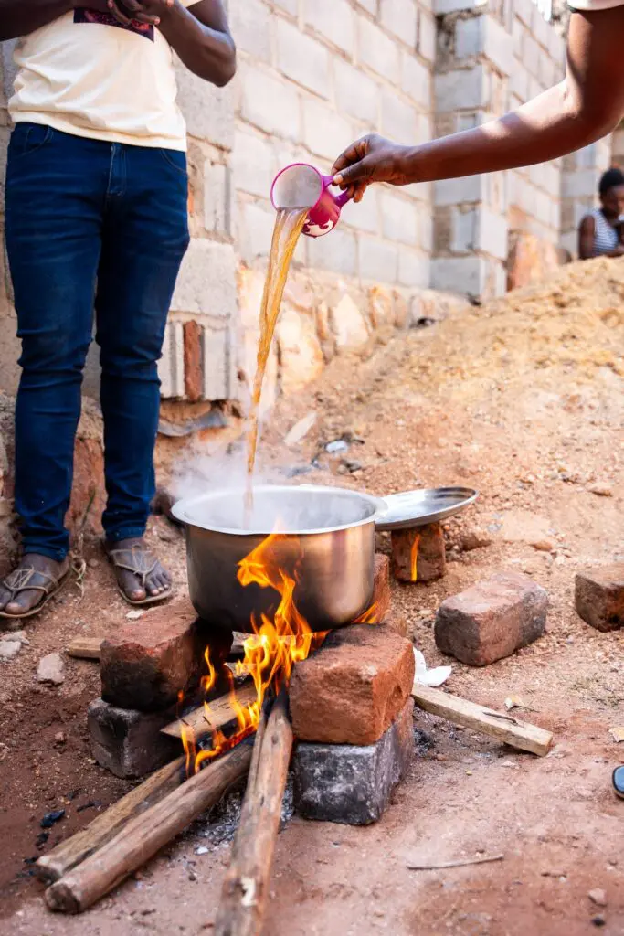person pouring liquid into pot over open fire in Uganda