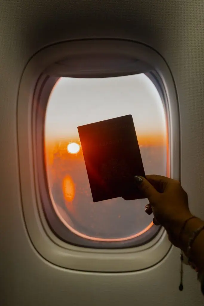 hand holding passport against airplane window sunset