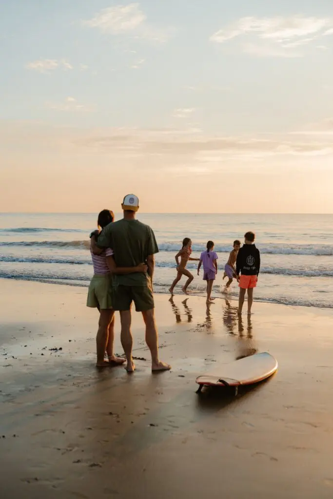 family watching kids play in ocean at sunset with surfboard