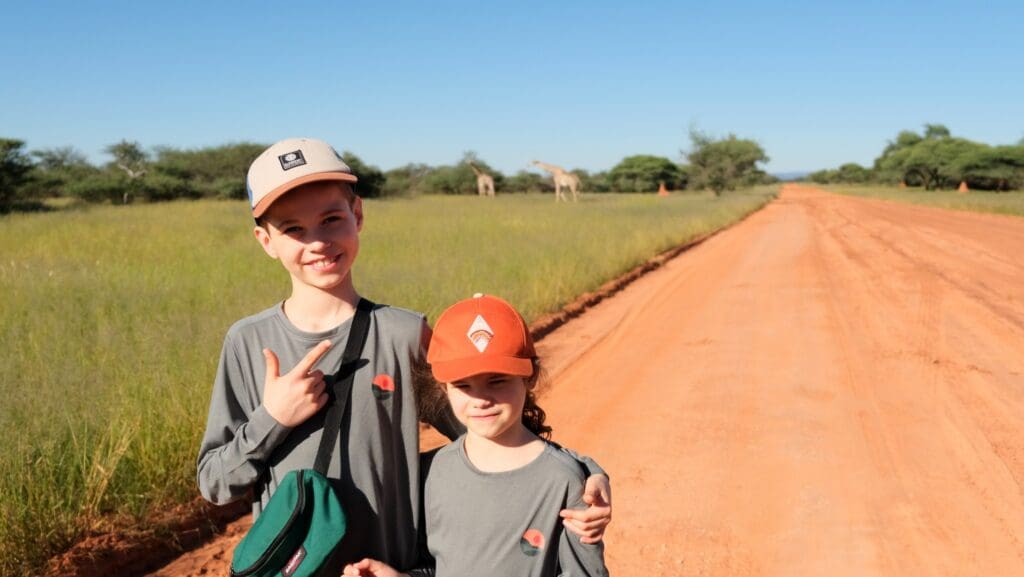 two children on a safari road with giraffes in background