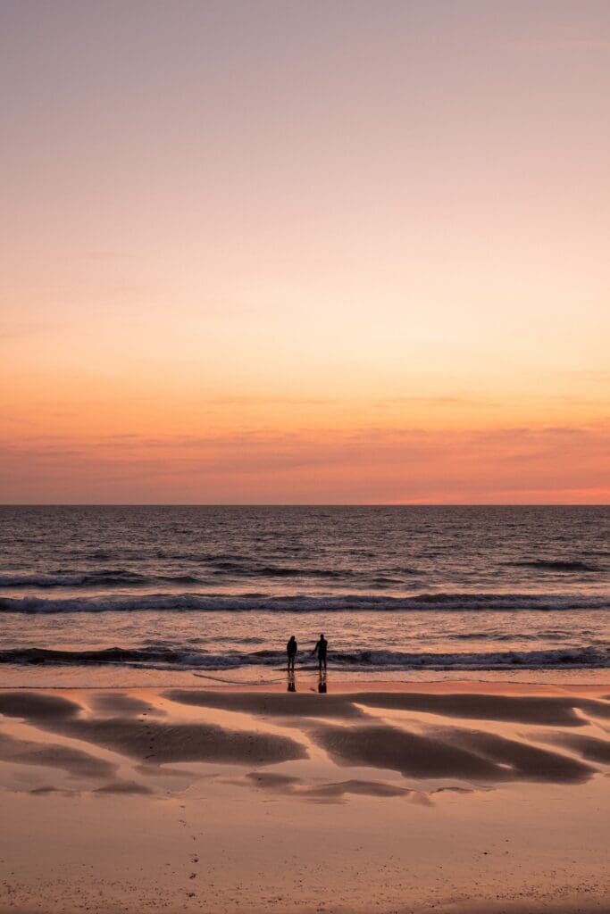 two people silhouetted on a beach at sunset