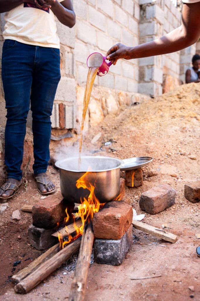 person pouring liquid into pot over open fire in Uganda