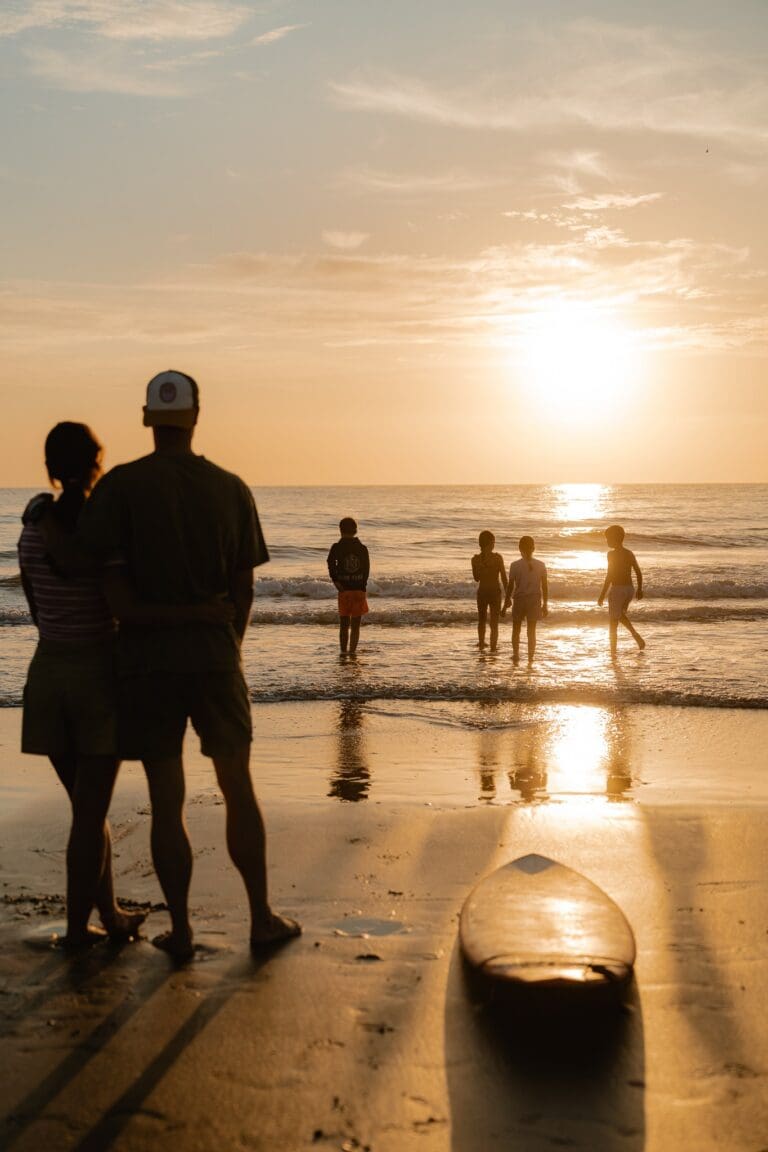 family watching sunset on beach with surfboard